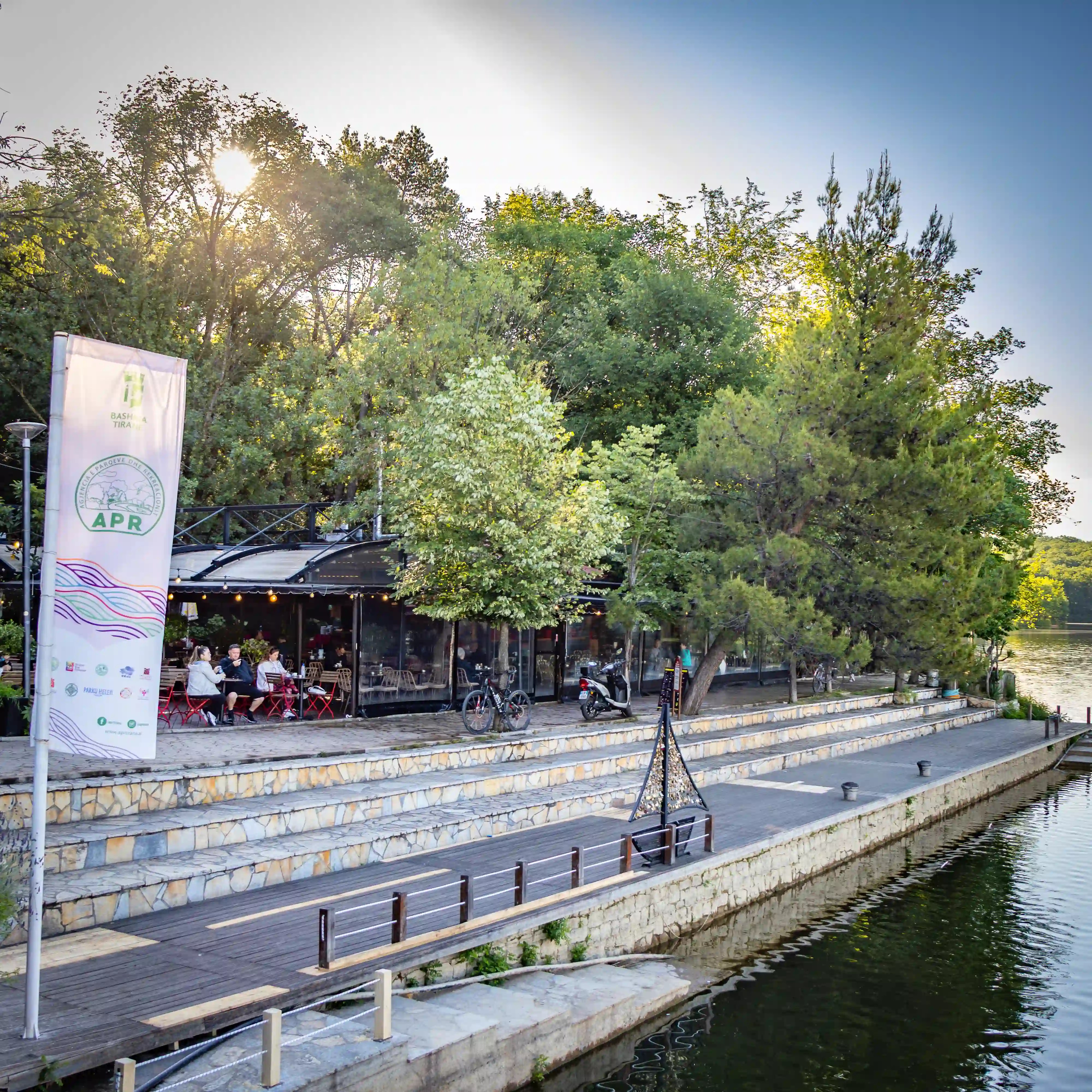 A lakeside cafe and promenade in Tirana's Grand Park during the early morning.